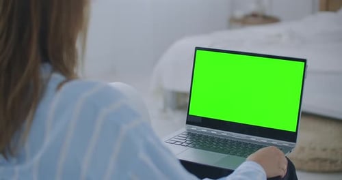 Young Woman at Home Works on a Laptop Computer with Green Mock-up Screen. She Sitting On a Couch in