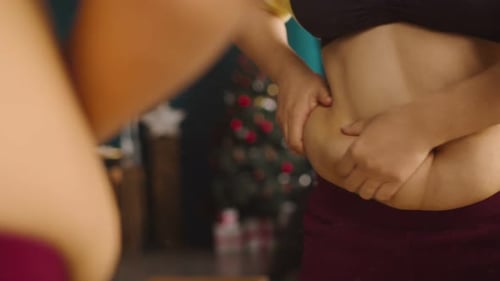 Mulher gorda toca sua barriga grande em pé na frente do espelho e mostrando excesso de peso
