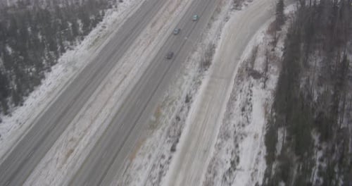 Aerial helicopter low shot over frozen river flowing past, green conifers on banks, flyover island t