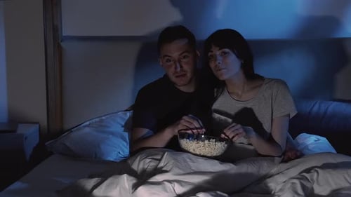 Couple Enjoying Movie Night in Bed Eating Popcorn