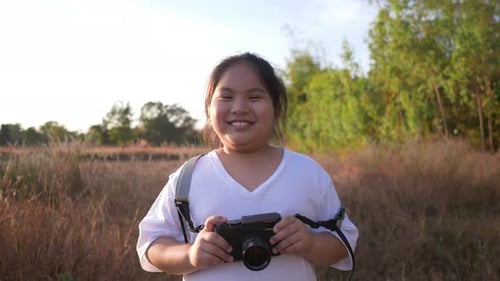 Front view of girl standing in meadow and holding a camera