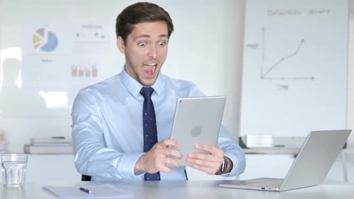 Young Man Celebrating Success with Tablet at Desk