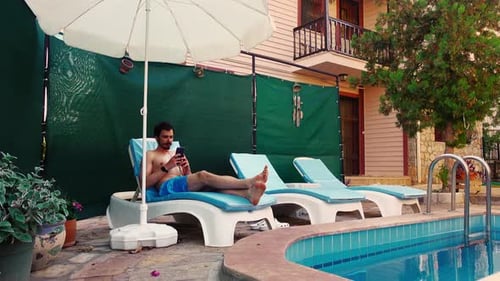 Young Man in Comes to Poolside in a Hotel Then Lies Down on a Lounge Chair and Starts Talking