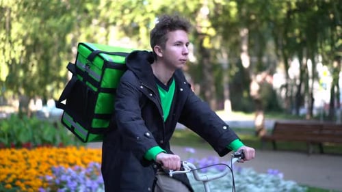 Livreur avec sac à dos vert fait du vélo à travers la ville avec livraison de nourriture