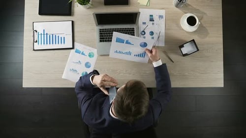 Business Person Looking at Graph and Talking Over Smartphone, Workplace Top View