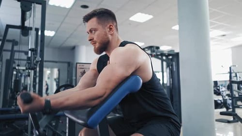 Bearded man pumping his arm muscles in the gym. Athletic bodybuilder training his biceps