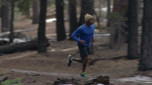 A young man trail running on a snow covered trail in a forest in the mountains.