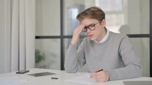 Young Man Reacting to Loss While Writing on Paper in Office