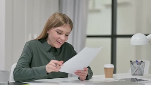 Woman Reviews Paperwork with Excitement at Desk