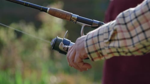 Close Up of Fishing Rod with Reel in Hands of Aged Angler