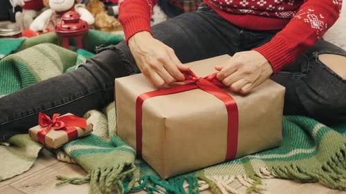 Young Adult Tying Red Ribbon on Christmas Gift