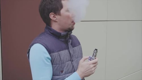 Un joven vapeador exhala grandes nubes de humo con una cámara lenta para vapear cigarrillos electrónicos