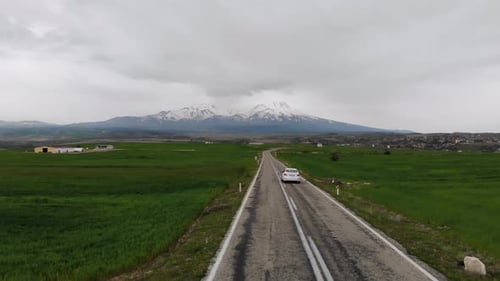 4K Aerial Drone Footage Of A Car Riding On A Road Between Green Fields