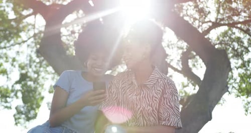 Two mixed race women look at smartphone in park