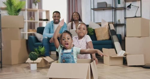 Padres sentados juntos y viendo cómo interpretan a sus dos hijas en una caja de cartón