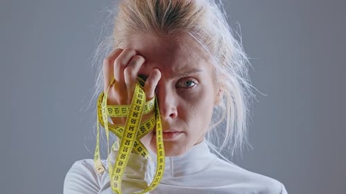 Modelo anoréxico que sostiene la cinta métrica