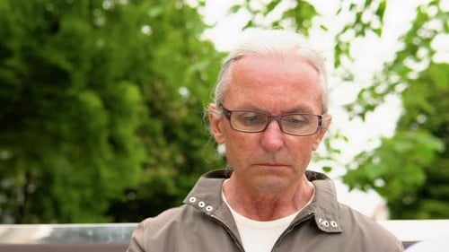Senior Man Reading Book Sitting on Bench in Park