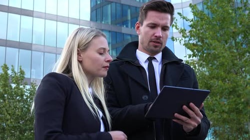 A Businessman and a Businesswoman Look at a Tablet and Talk - View From Below - an Office Building