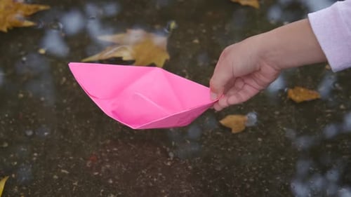Child Launches Pink Paper Boat in Autumn Puddle
