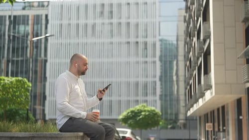 Man Sits, Drinks Coffee, Uses Phone in City