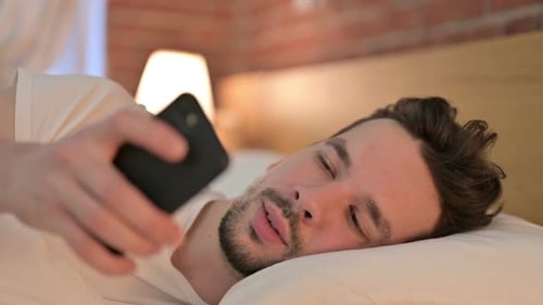 Man Lying in Bed Holding Mobile Phone Indoors