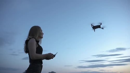 Junges Mädchen steuert Quadcopter-Drohne, die mit Fernbedienung unter blauem Himmel in der Luft fliegt