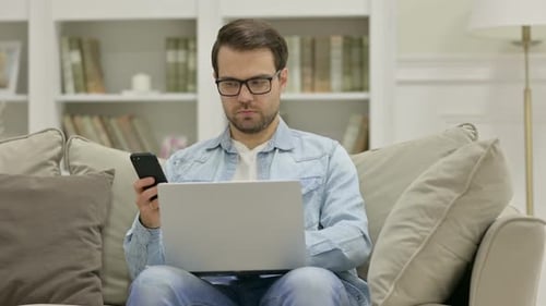 Man Uses Laptop and Smartphone on Sofa