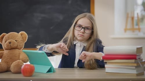 Dissatisfied Caucasian Schoolgirl Gesturing Thumbs Down Looking at Camera with Tired Facial