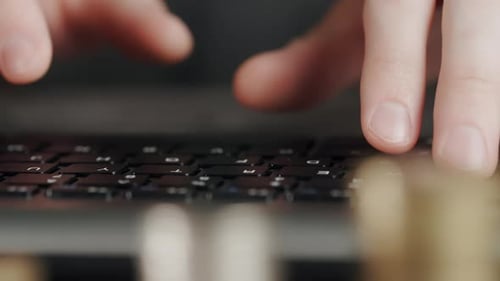 Fingers Typing on Computer Keyboard near Stacks of Coins