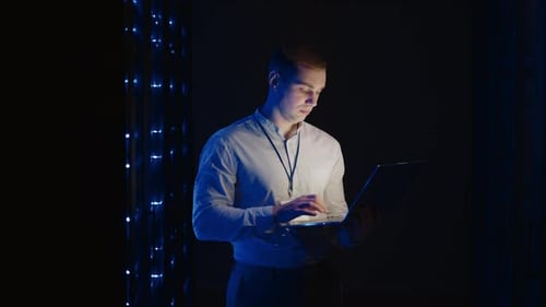 Junger Mann hält das Gerät in der Hand und schaut auf den Bildschirm, inspiziert Ausrüstung oder Hardware-Rack
