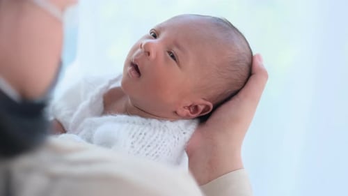 Close up and portrait of newborn baby is held by mother with mask and baby look look to mother