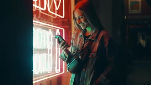 Woman Using Smartphone Next to Neon Lights at Night