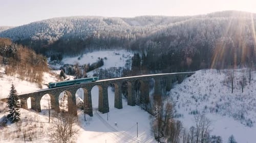 Train de voyageurs traversant un viaduc en pierre, paysage enneigé, de gauche à droite.