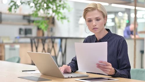 Beautiful Young Businesswoman Working on Laptop with Documents in Office