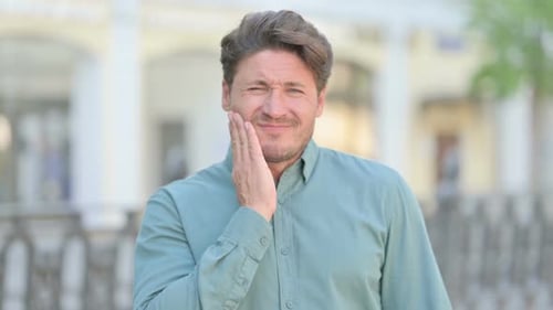Man with Toothache Holding Jaw in an Outdoor Setting