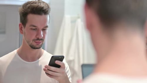 Young Adult Using Phone in Bathroom Mirror