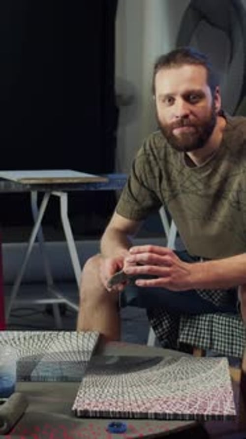 Um artista está segurando em suas mãos um pincel e olhando para a câmera