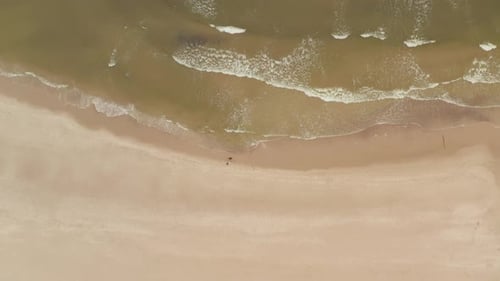 Foto de una pareja o amigos caminando por la playa con olas rompiendo