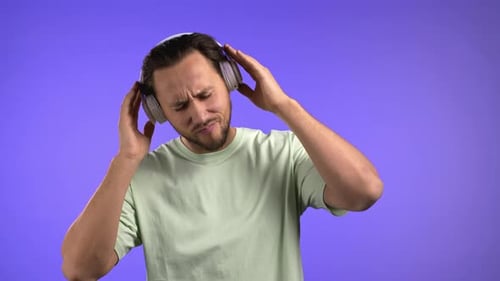 Handsome Young Man Enjoy Music Smiling with Headphones in Studio Against Violet Background