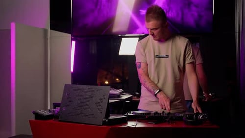DJ working on stage in club indoors. Young adult man using console for mixing music list