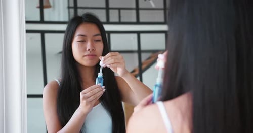 Woman Applying Facial Serum in Mirror, Beauty Routine