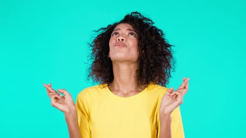 Woman Hopeful with Fingers Crossed on Teal Background