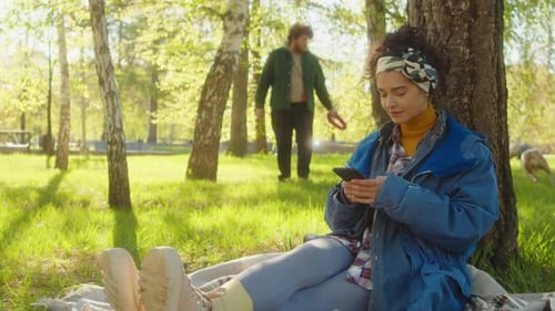 Woman Using Smartphone and Petting Corgi in Park