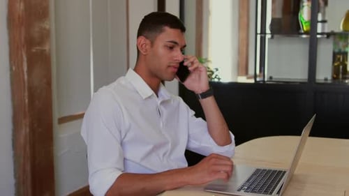 Young Adult Talks on Phone While Using Laptop