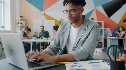 Serious Afro-American Man Using Laptop Then Writing Notes Working in Modern Office