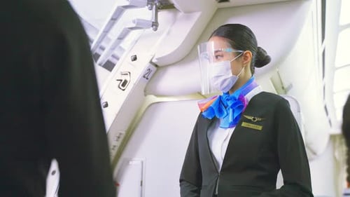 Mujer azafata asiática con máscara facial saludando a los pasajeros que caminan a bordo en un avión.