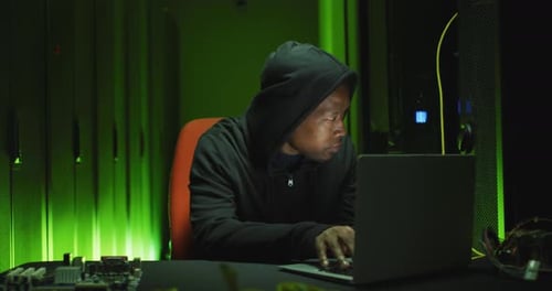 Un pirate informatique afro-américain utilise un ordinateur portable dans une salle de serveurs d'entreprise