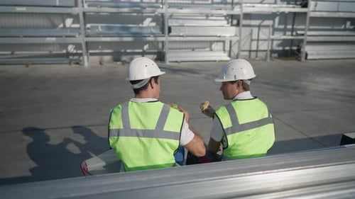 Back View of Two Positive Workers Eating Lunch Talking in Slow Motion Sitting at Warehouse Outdoors