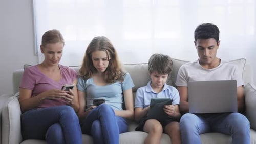 Family Using Electronic Devices on Couch at Home
