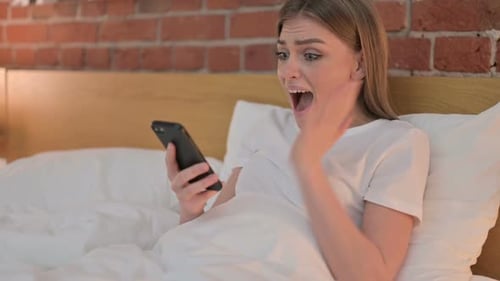 Woman in Bed Looking at Cellphone Happy